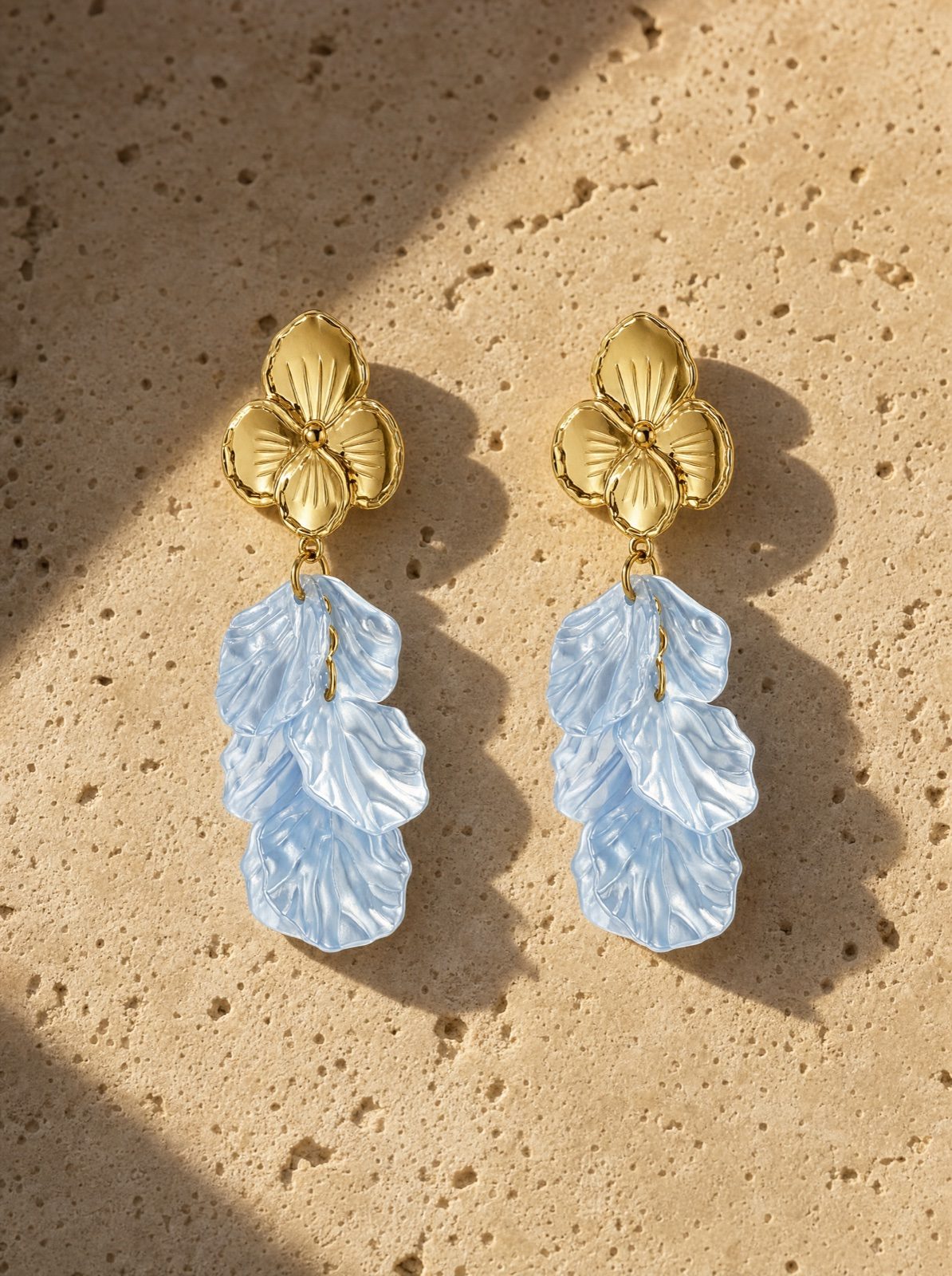 flower earrings in mother of pearl, baby blue, on travertine stone in afternoon light