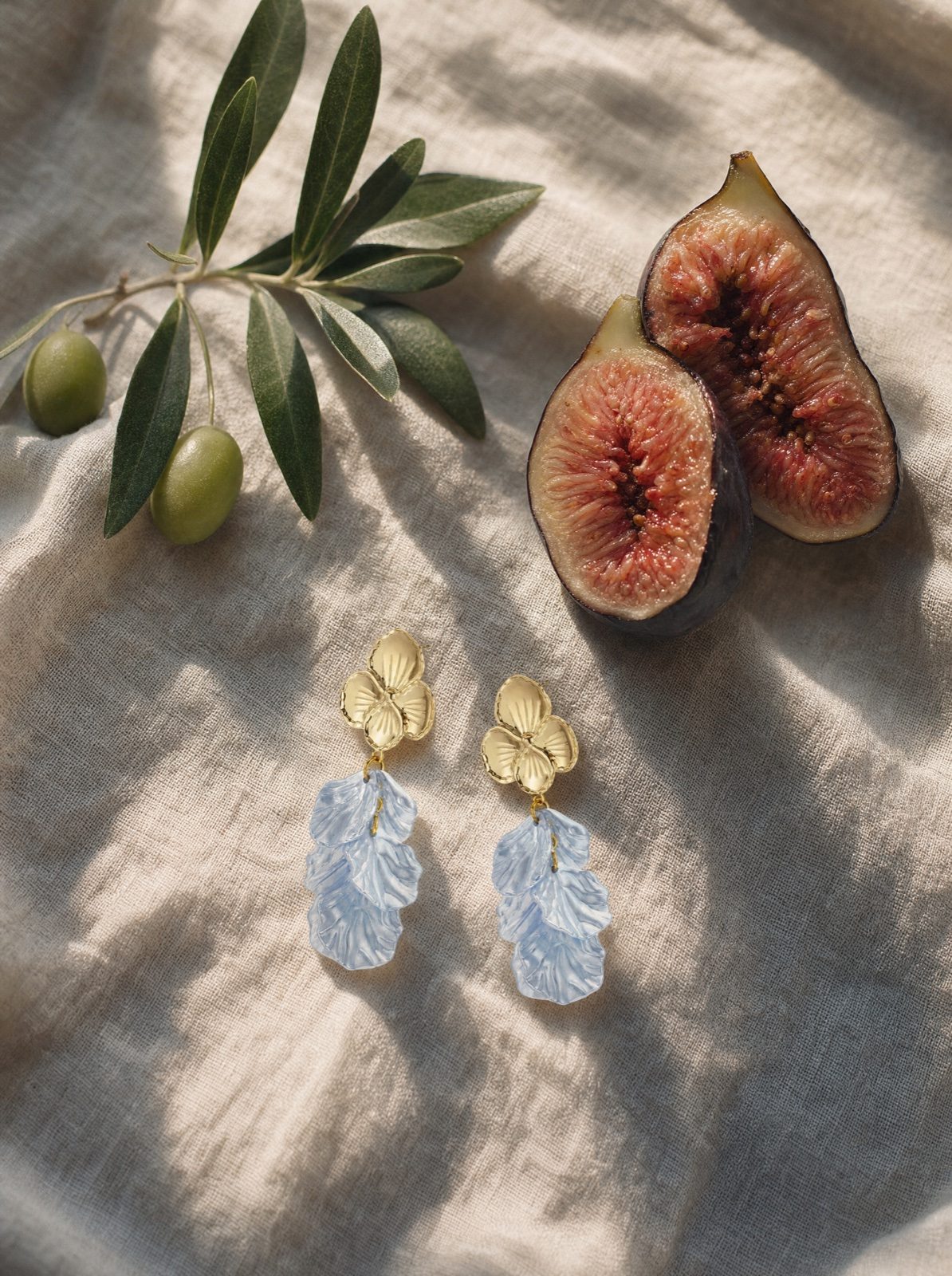 flower earrings in mother of pearl, baby blue, on cream linen with an olive branch and halved figs