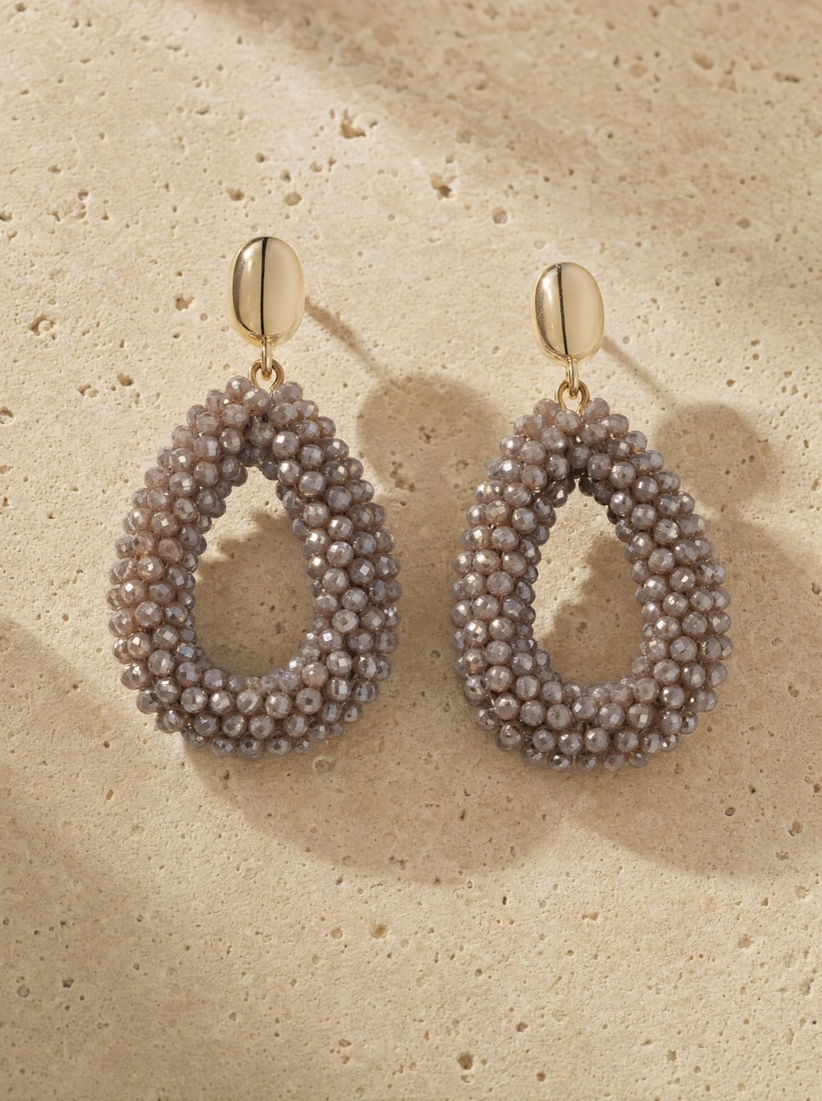 amalfi drops, brown faceted crystal beads with a gold-tone stud, on travertine stone in afternoon light