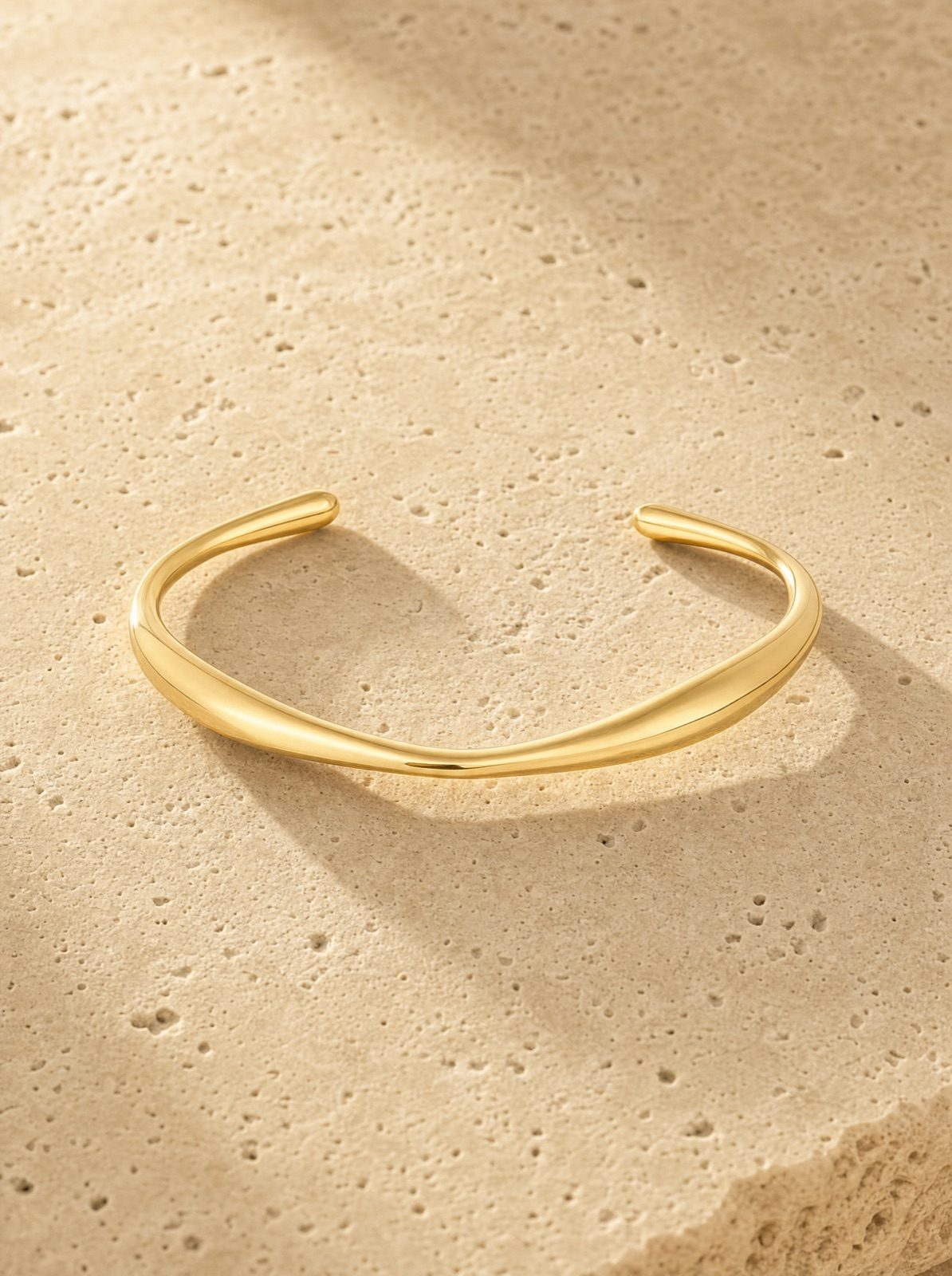 organic open cuff in gold stainless steel on travertine stone in afternoon light