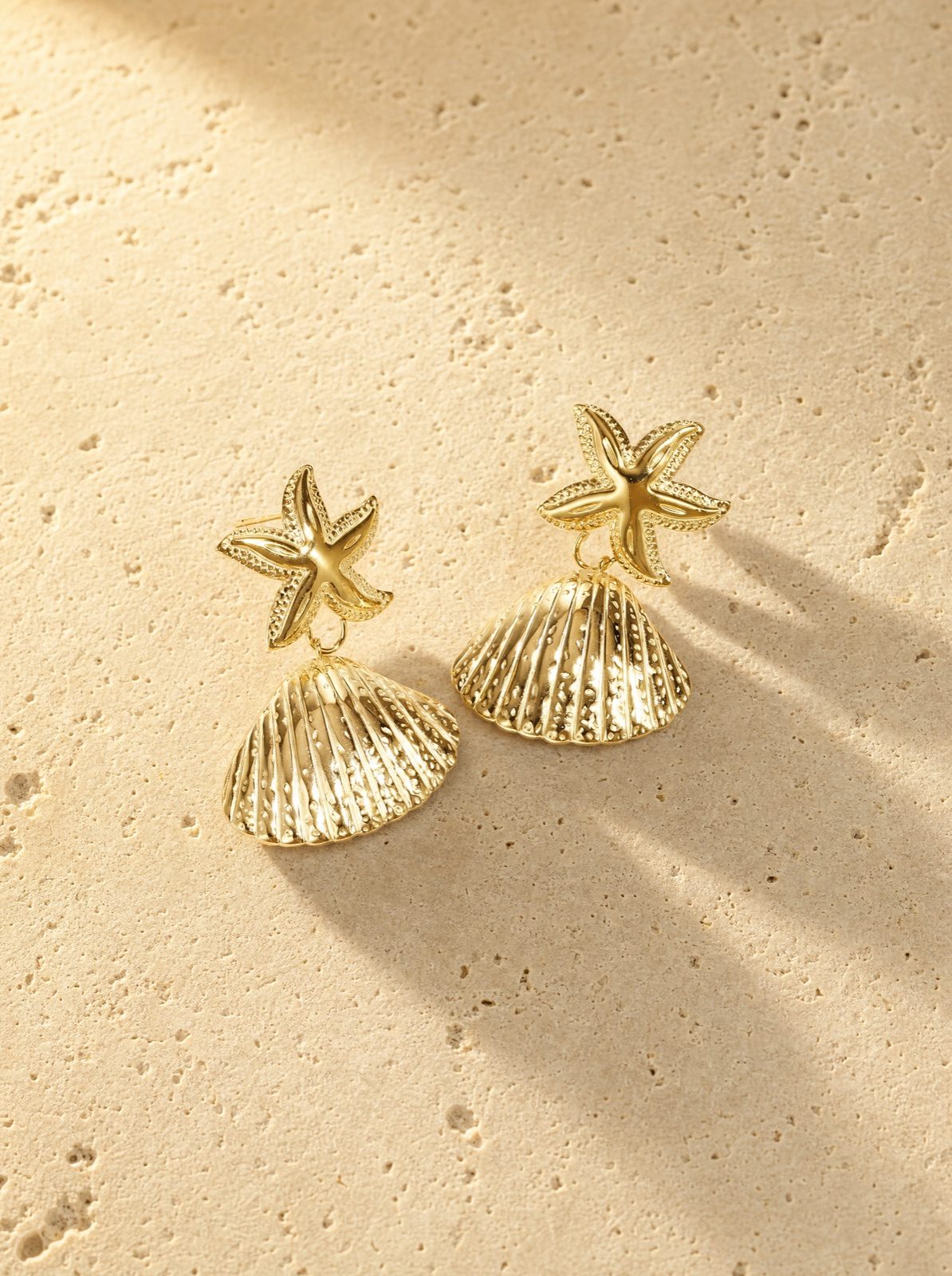 shell and starfish studs in gold stainless steel on travertine stone in afternoon light
