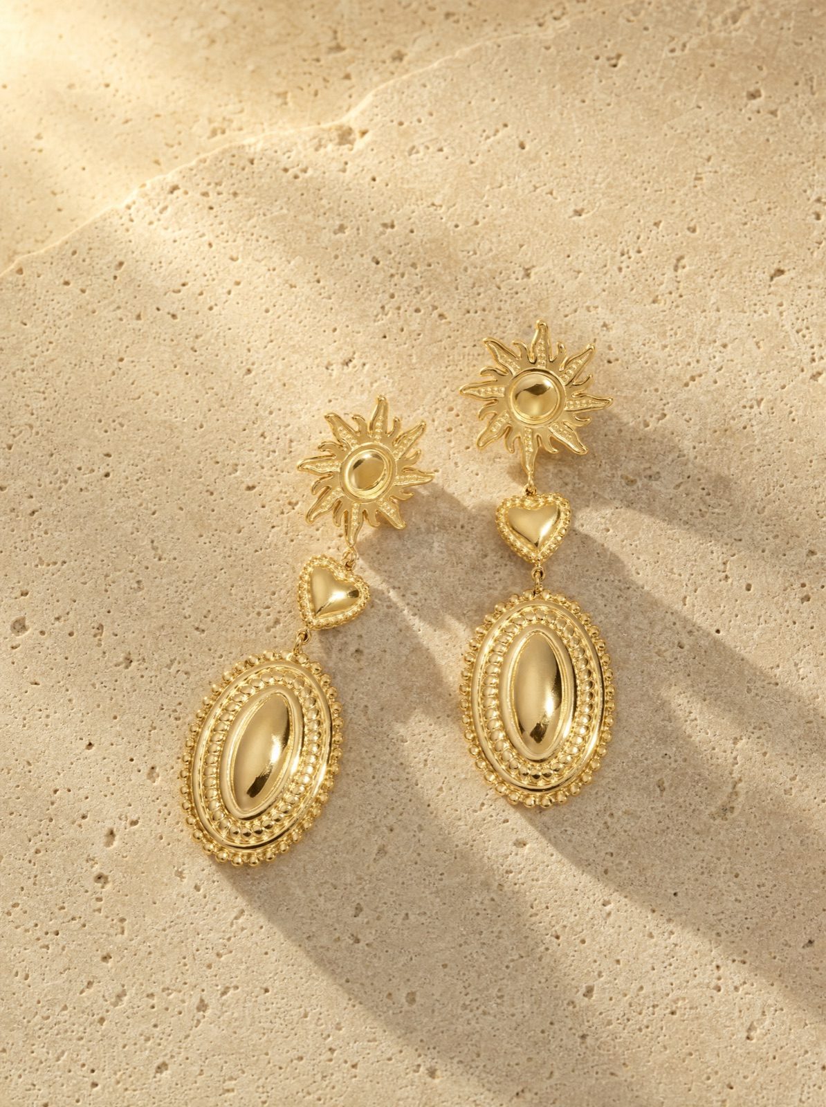 sun and heart drop earrings in gold stainless steel on travertine stone in afternoon light
