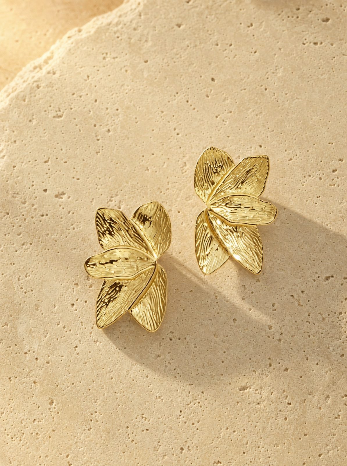 leaf studs in gold stainless steel on travertine stone in afternoon light