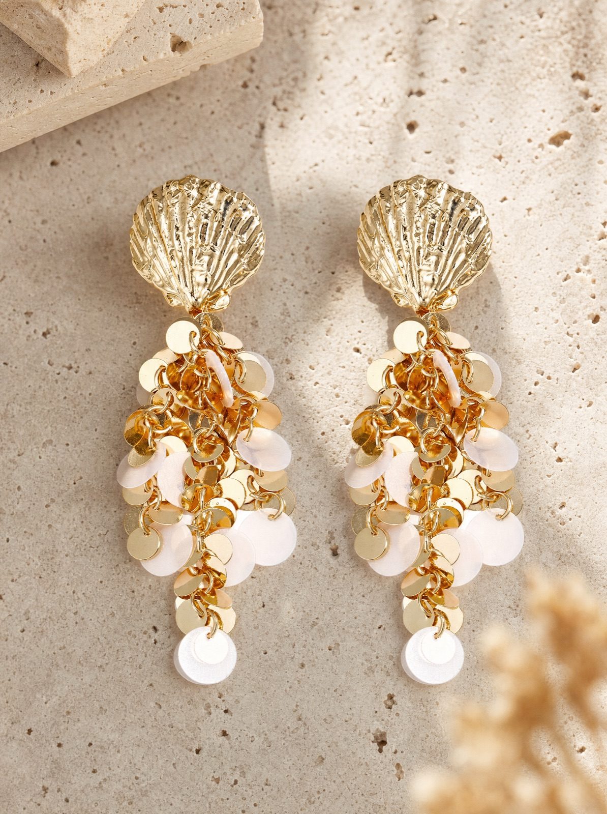 shell earrings with hanging gold sequins on travertine stone in afternoon light