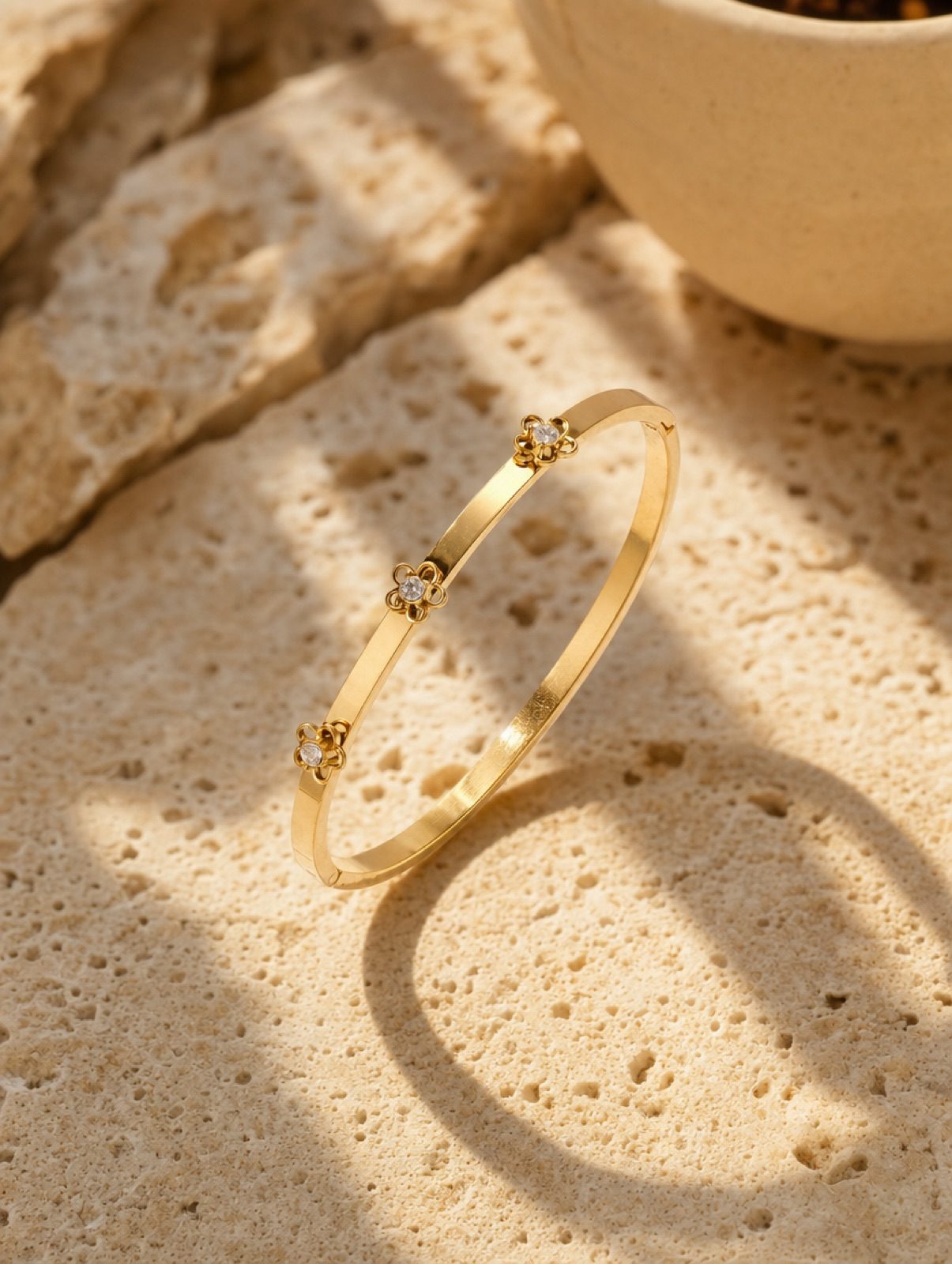 fiore bangle in gold, a slim flower band set with clear rhinestones, on travertine stone in afternoon light