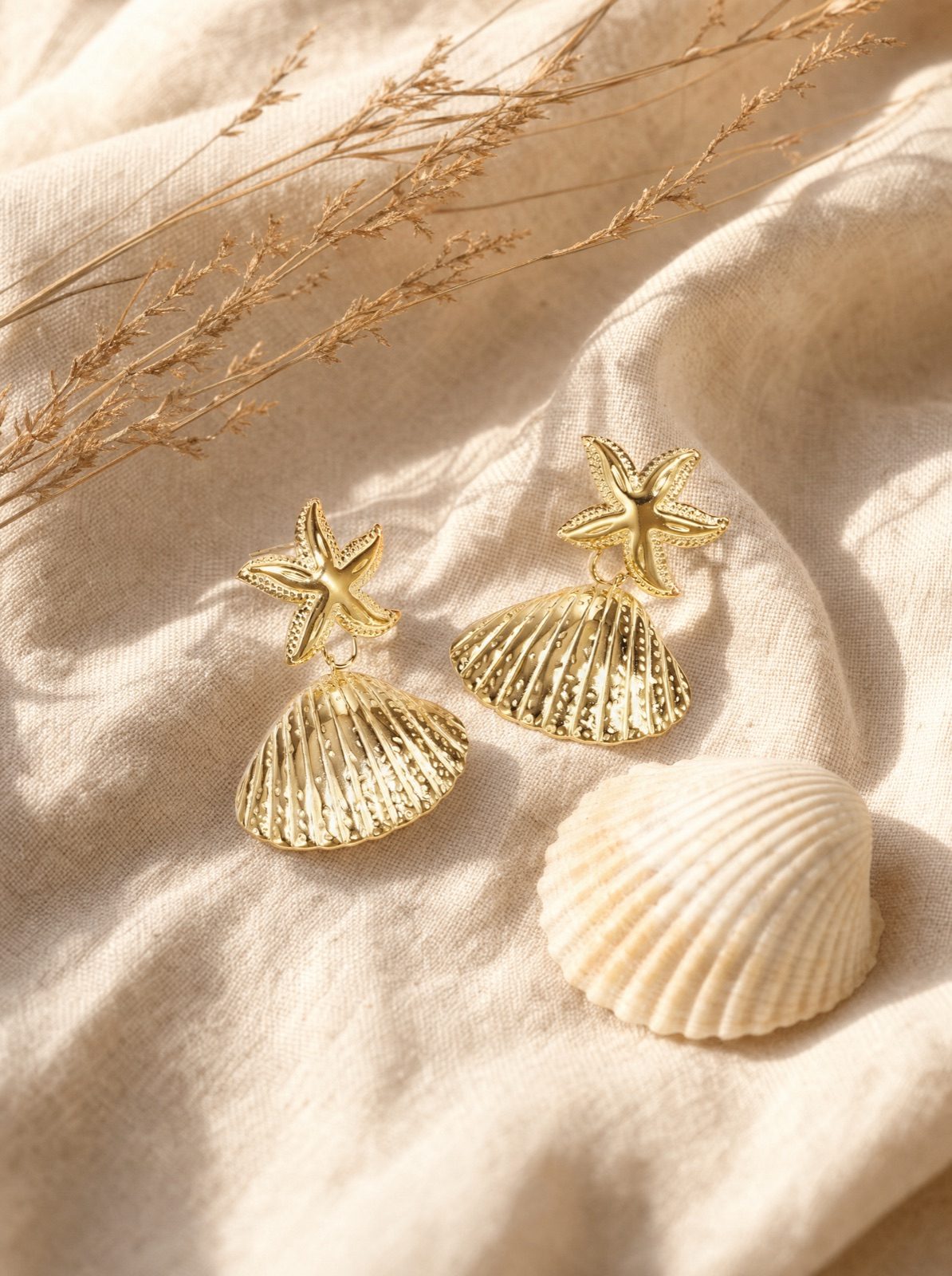 shell and starfish studs in gold on cream linen beside a small shell