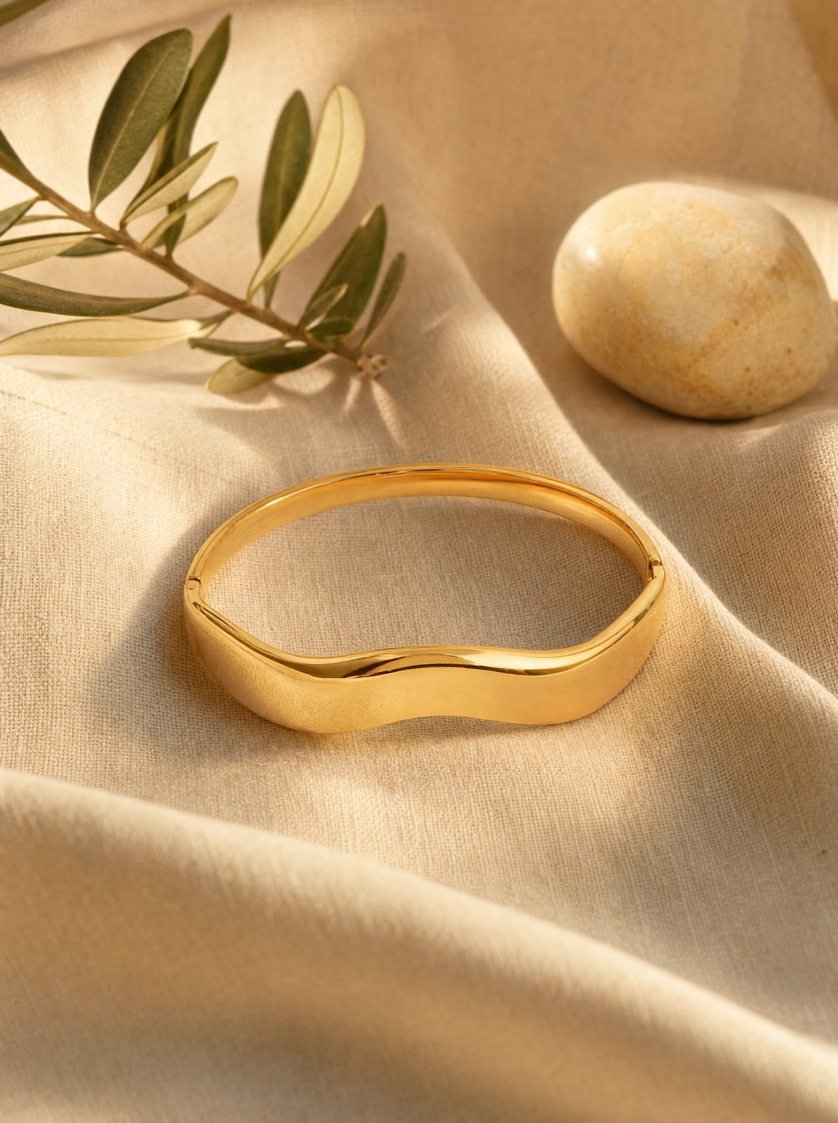 wavy bangle in gold on cream linen with an olive branch