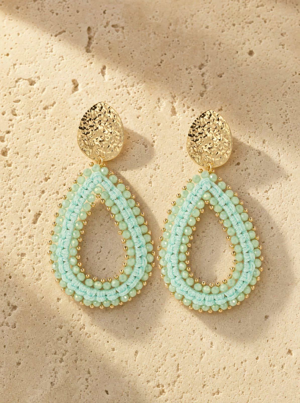 riviera drops, mint-green woven crystal beads with a gold-tone stud, on travertine stone in afternoon light