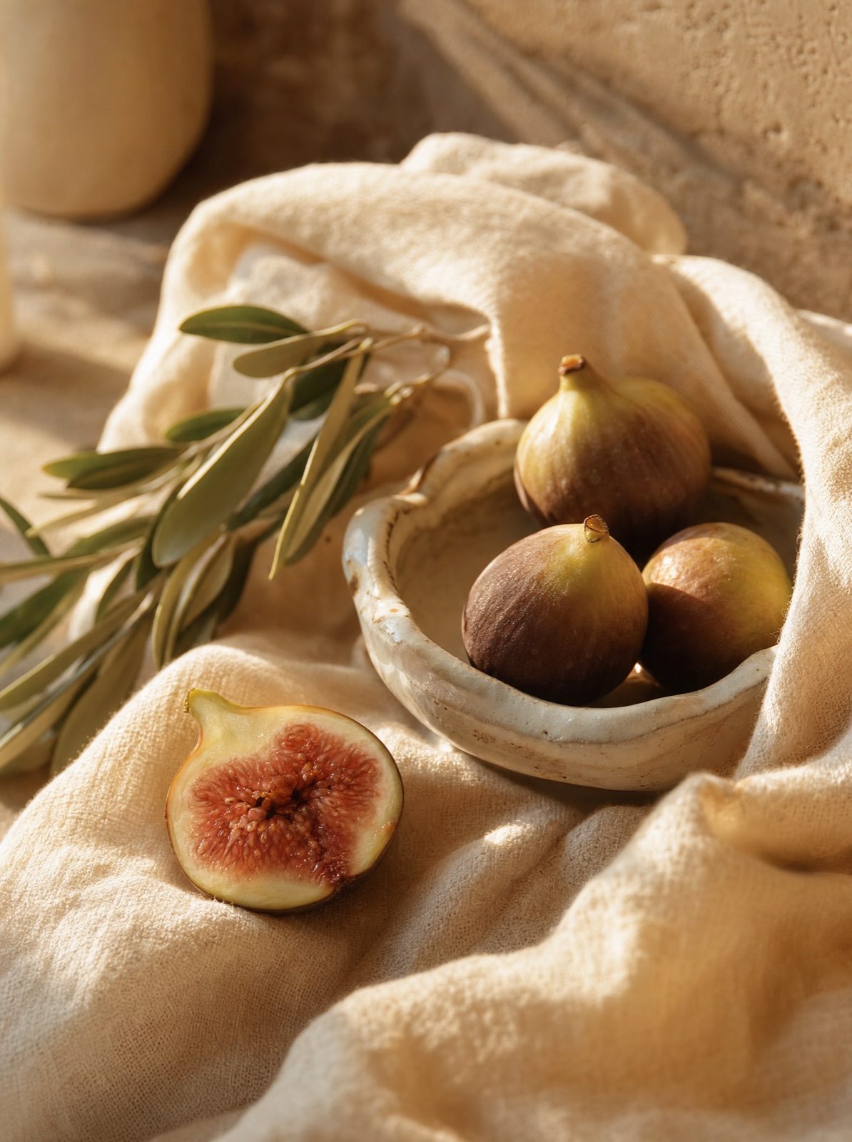 halved figs on cream linen beside an olive branch in warm afternoon light