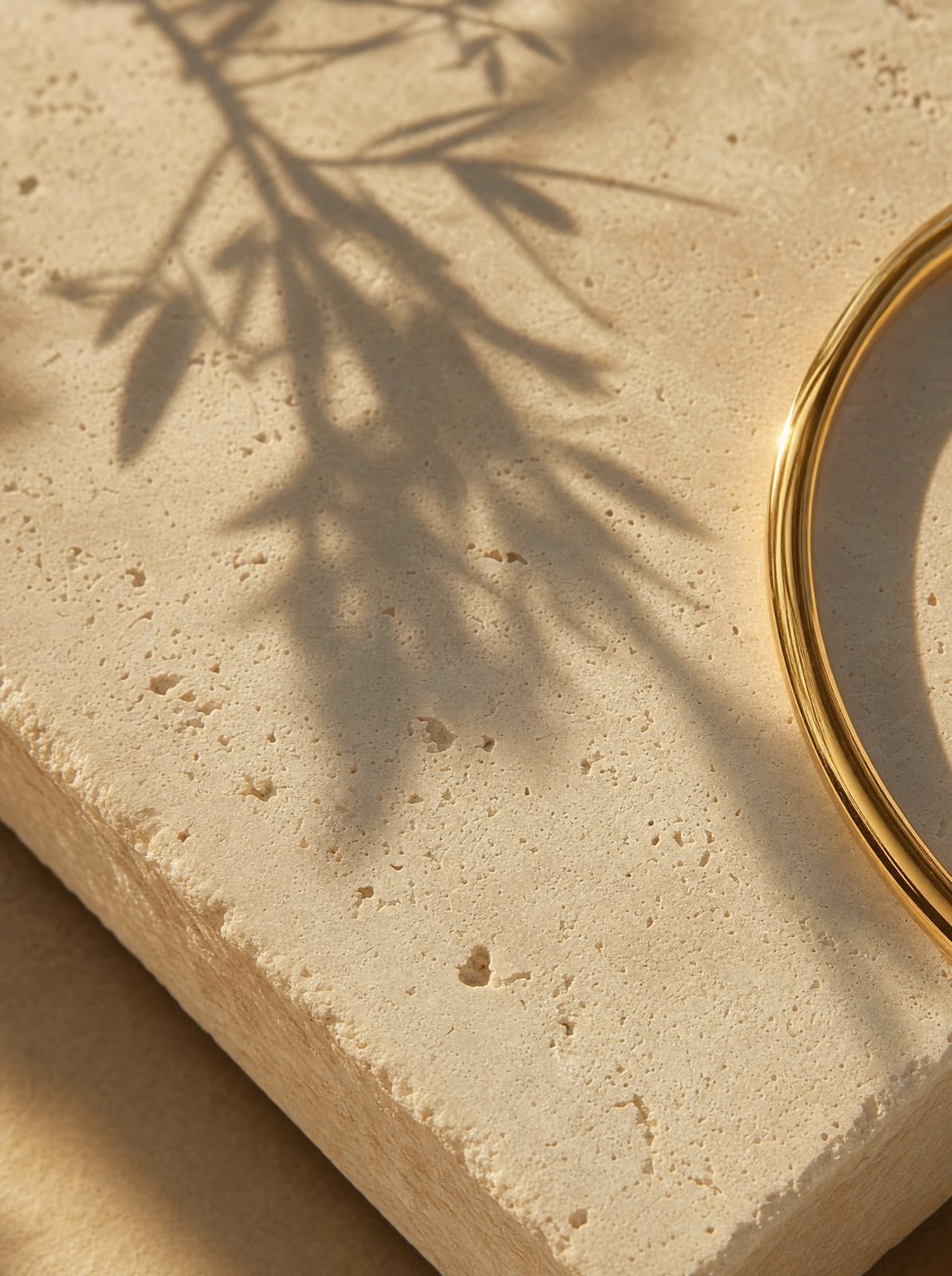 gold-tone stainless steel jewellery resting on warm travertine stone