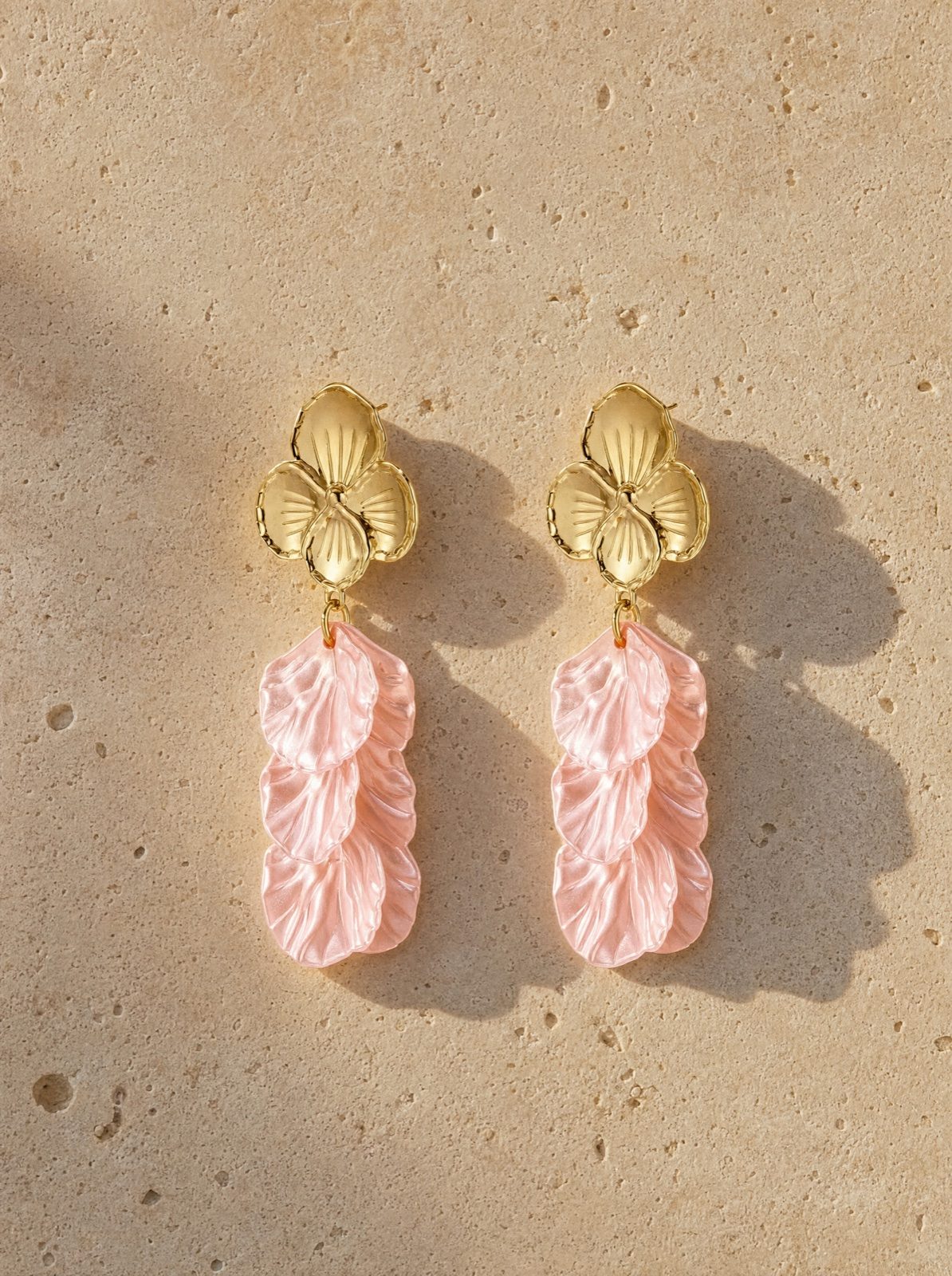 flower earrings in mother of pearl, light pink, on travertine stone in afternoon light
