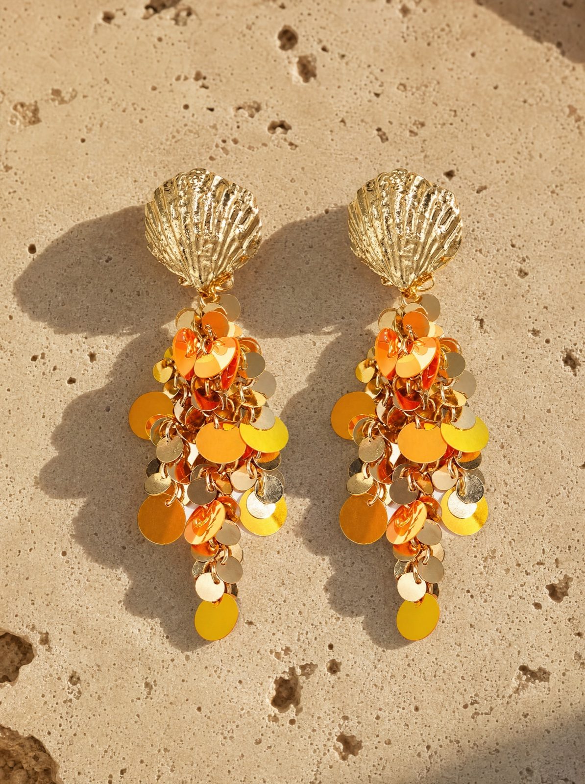 shell earrings with hanging orange sequins on coral stone in afternoon light