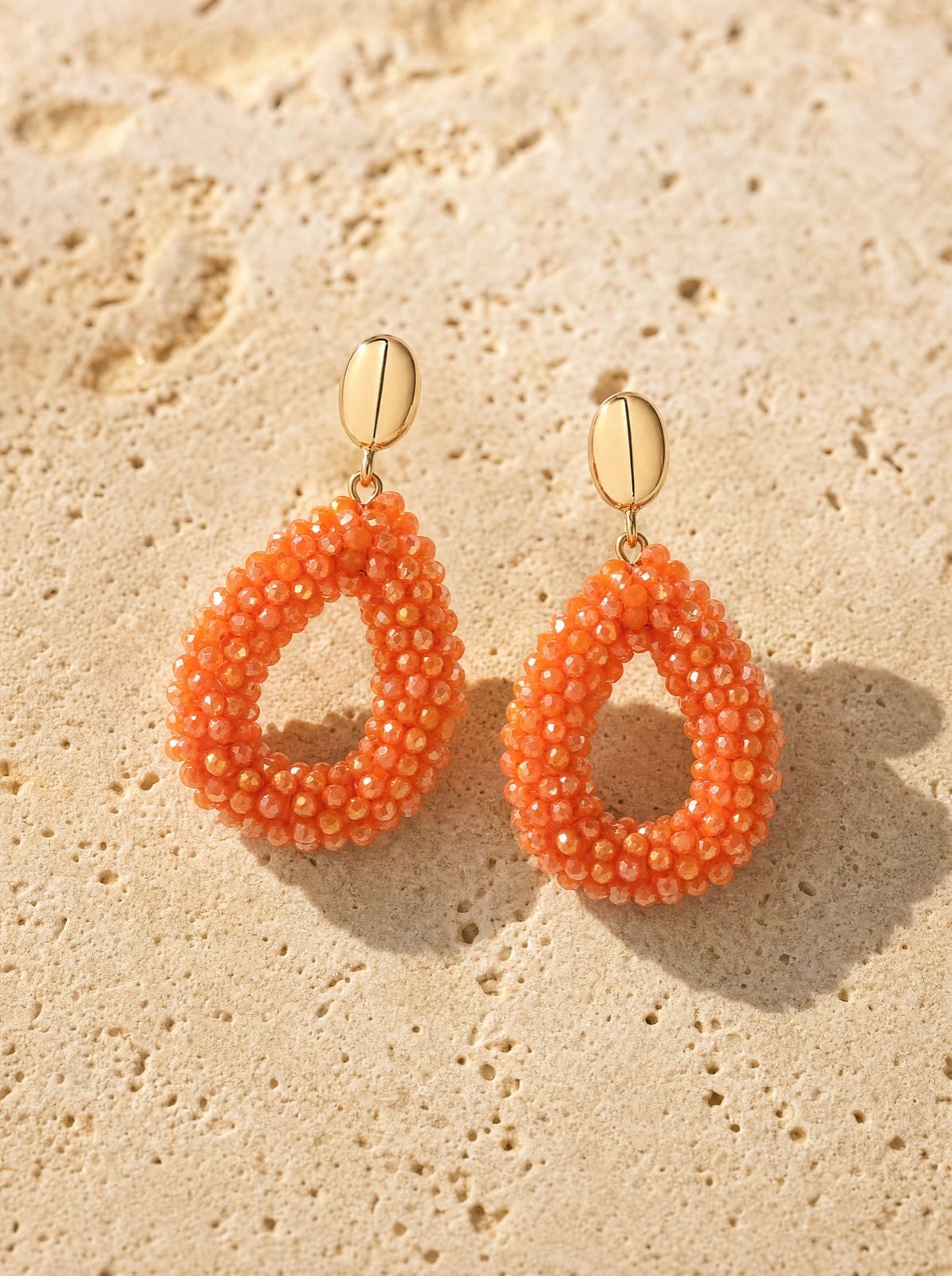 amalfi drops, orange faceted crystal beads with a gold-tone stud, on travertine stone in afternoon light
