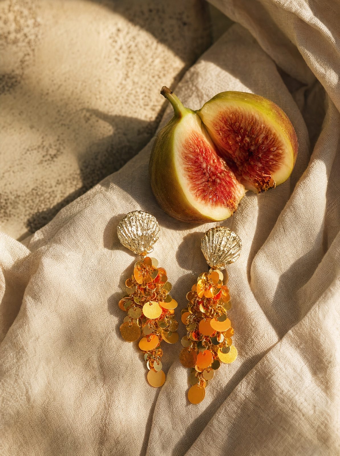 shell earrings with hanging orange sequins on cream linen with a halved fig
