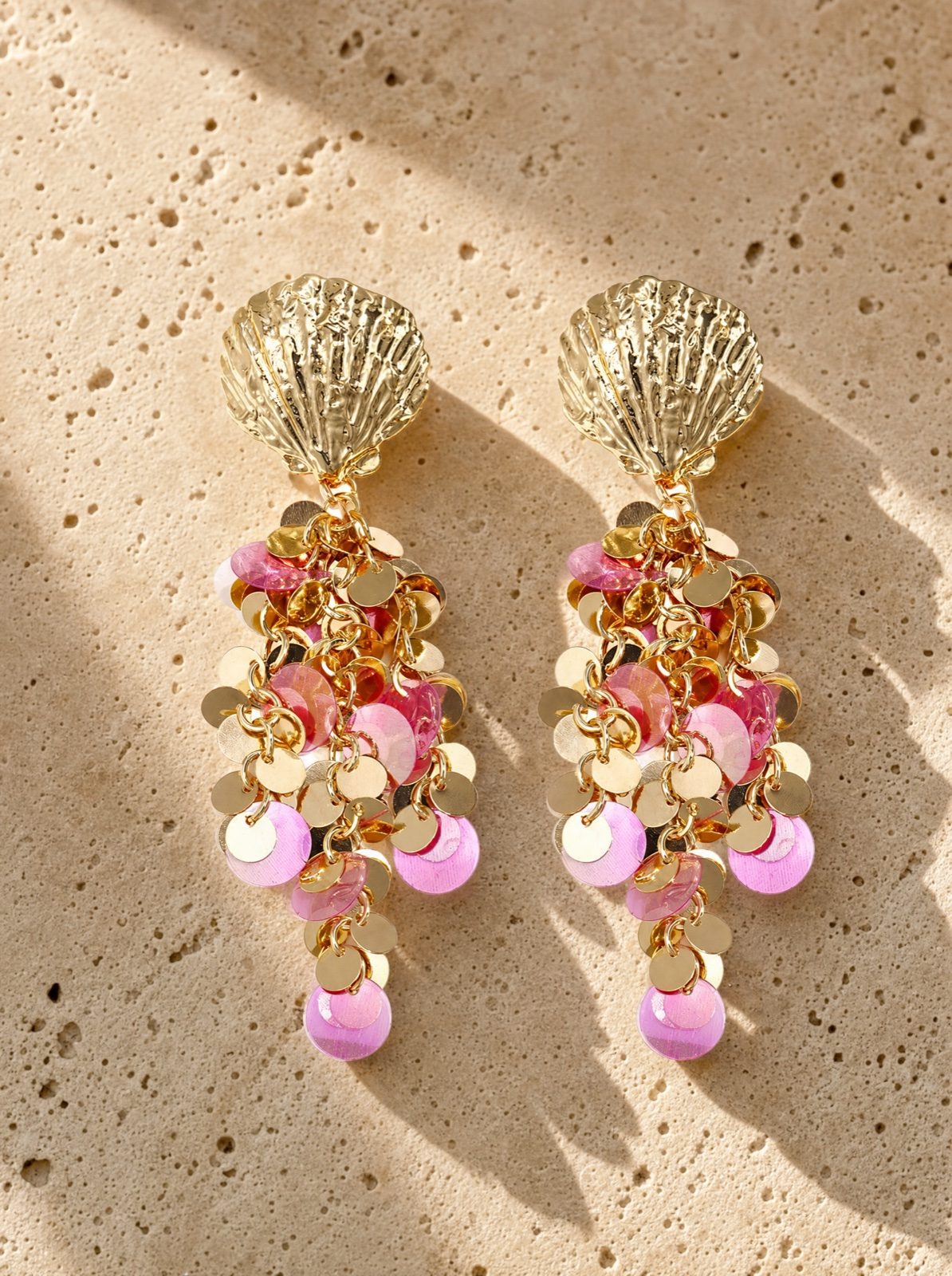 shell earrings with hanging pink sequins on coral stone in afternoon light
