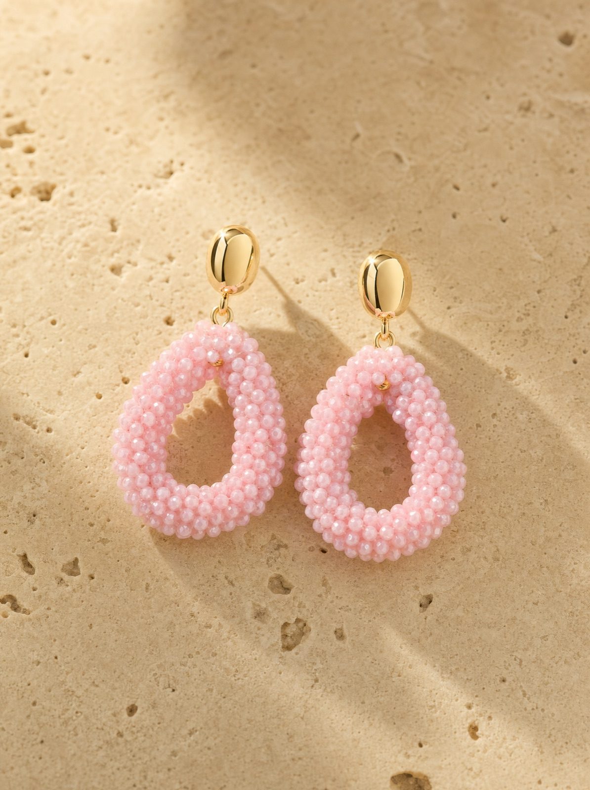 amalfi drops, pink faceted crystal beads with a gold-tone stud, on travertine stone in afternoon light