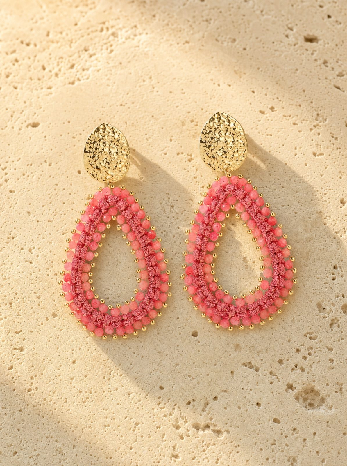 riviera drops, coral woven crystal beads with a gold-tone stud, on travertine stone in afternoon light