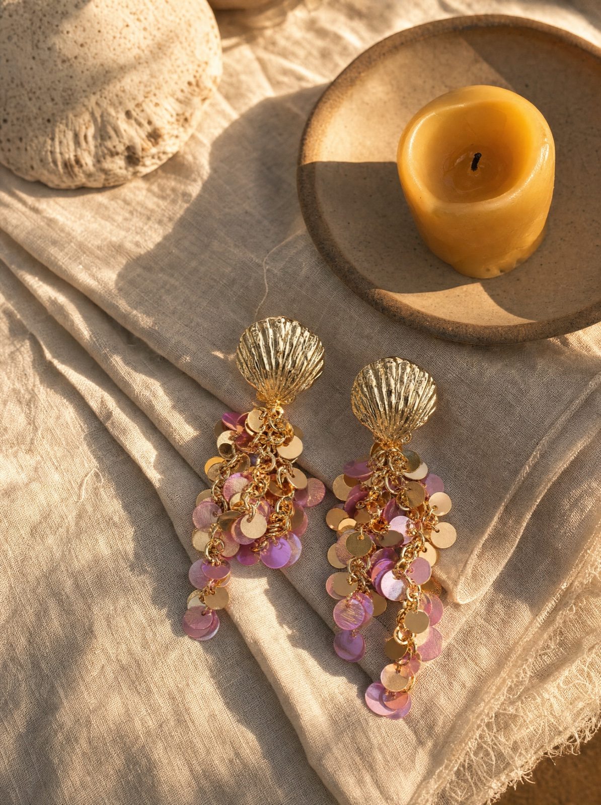 shell earrings with hanging pink sequins on cream linen with a beeswax candle on a small wooden plate