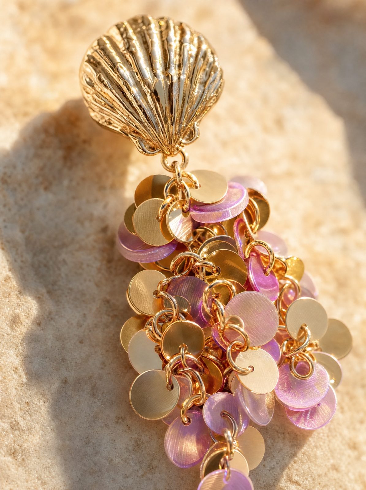 macro detail of a single shell earring with hanging pink sequins on a sandy stone