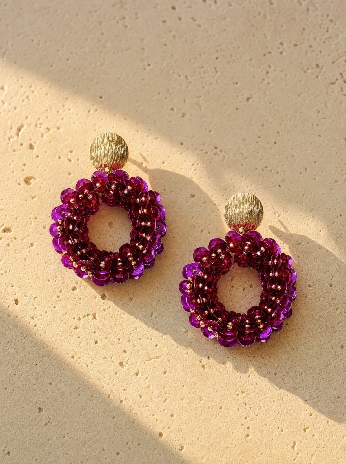 sequin drop earrings in purple on travertine stone in afternoon light