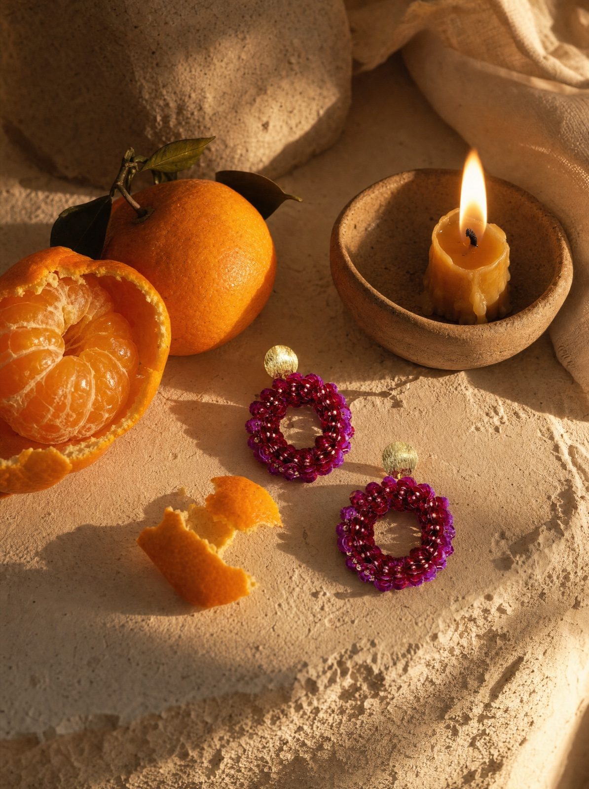 sequin drop earrings in purple on cream linen with peeled oranges and a small beeswax candle