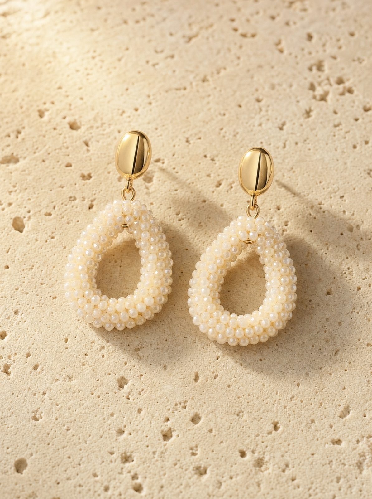 amalfi drops, rice-white faceted crystal beads with a gold-tone stud, on travertine stone in afternoon light