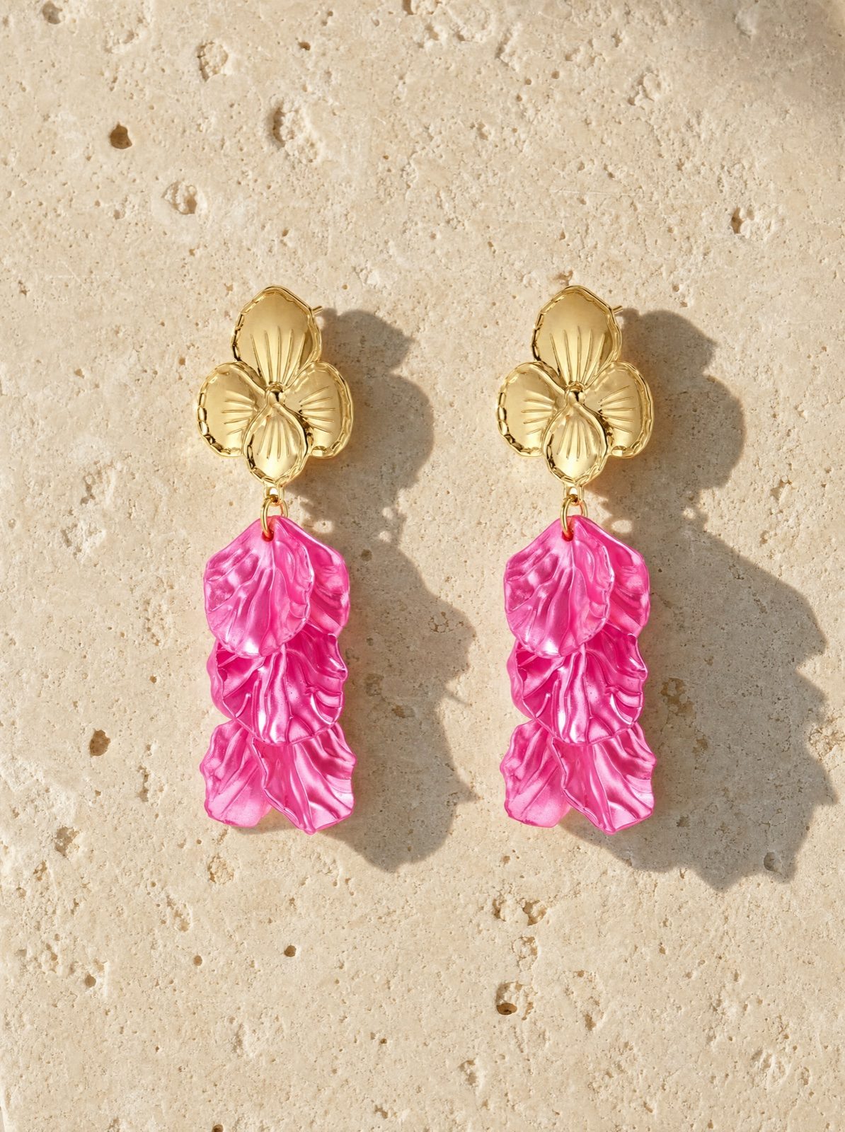flower earrings in mother of pearl, rose red, on pale stone in raking afternoon light