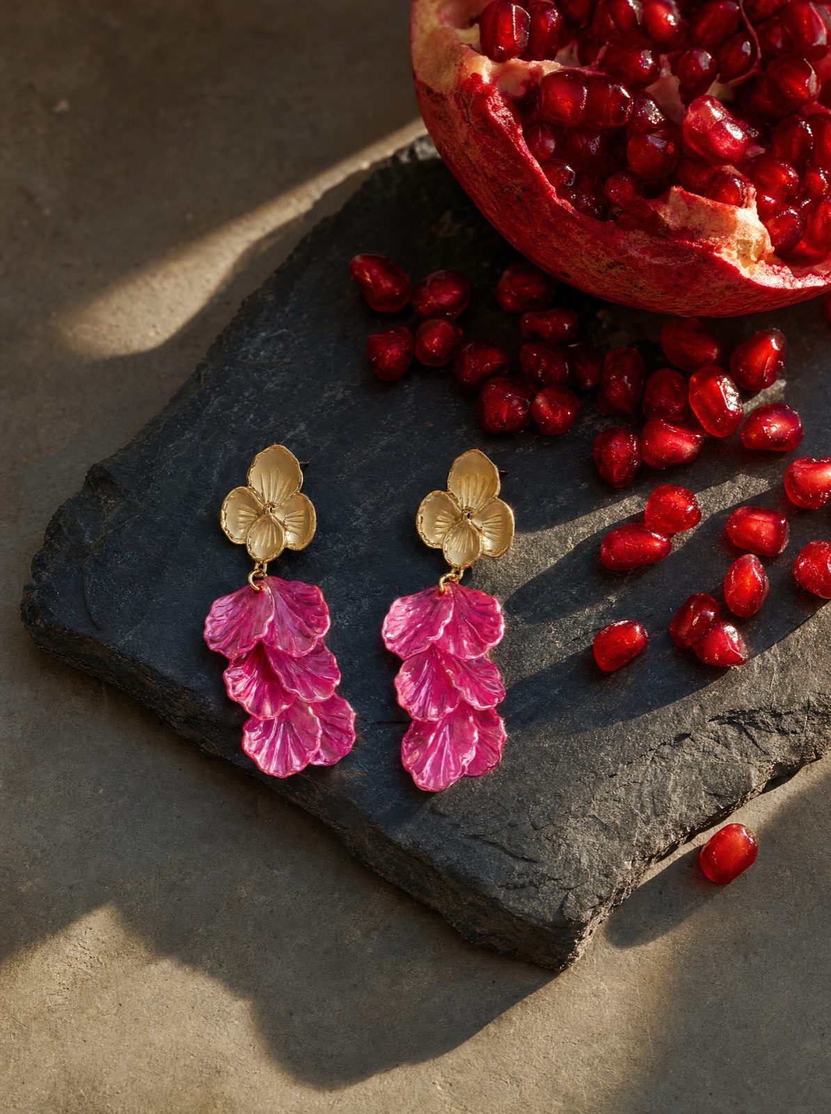 flower earrings in mother of pearl, rose red, on slate with a halved pomegranate and scattered seeds