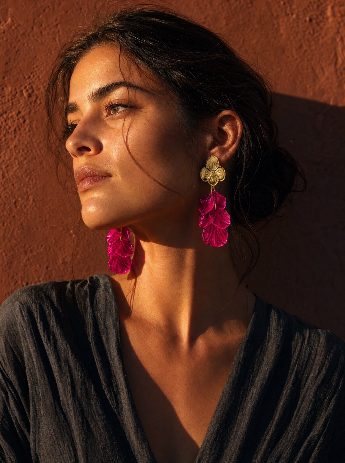 woman wearing the flower earrings in mother of pearl, rose red, in sun-lit profile against a terracotta wall