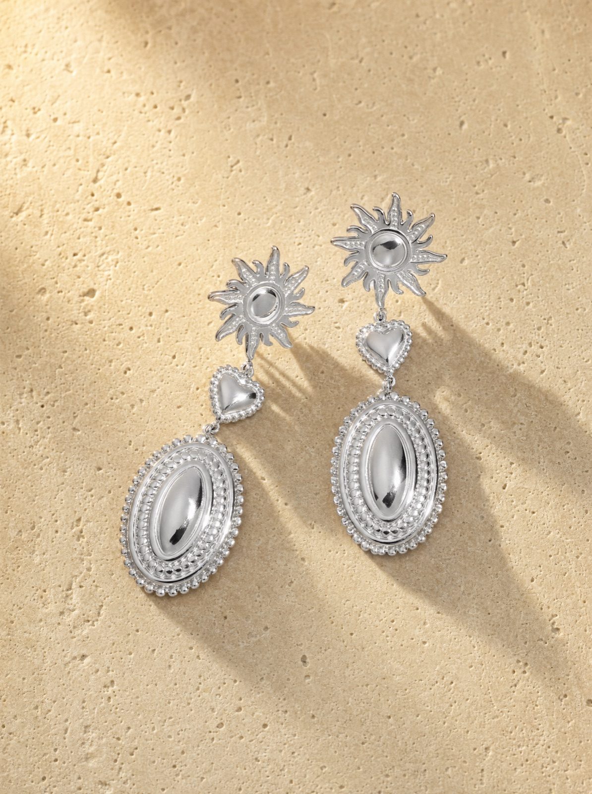 sun and heart drop earrings in silver stainless steel on travertine stone in afternoon light