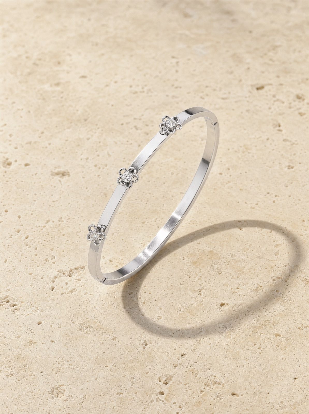 fiore bangle in silver, a slim flower band set with clear rhinestones, on travertine stone in afternoon light