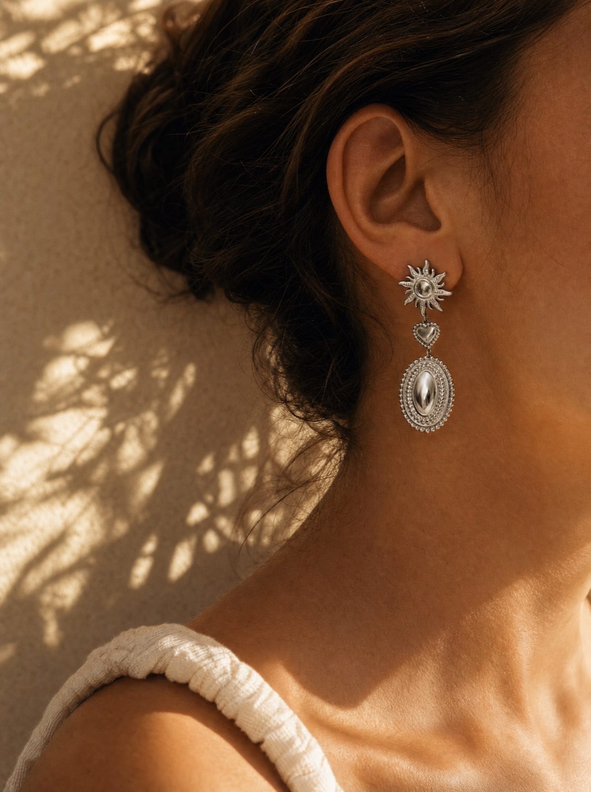 woman wearing the sun and heart drop earrings in silver, side profile