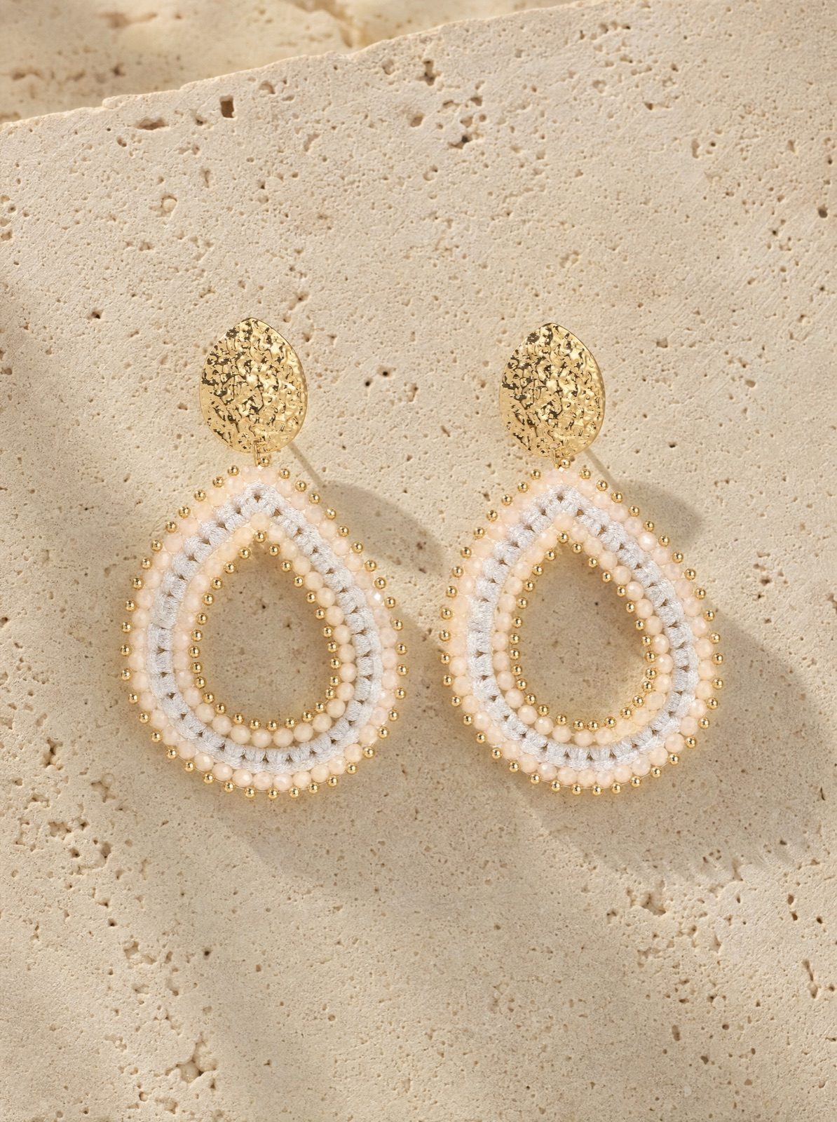 riviera drops, pearl-white woven crystal beads with a gold-tone stud, on travertine stone in afternoon light